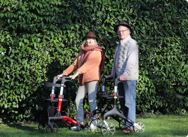 Two older adults standing outdoors with rollator walkers